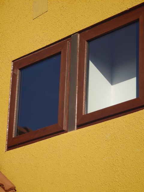 Ventanas de PVC abatibles color nogal en fachada amarilla